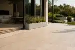 Duża prostokątna donica z roślinami ozdobnymi na tarasie przy przeszklonej ścianie domu.