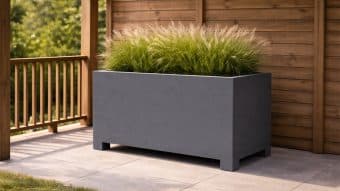 Donica aluminiowa Apollo 20, duża prostokątna biała aluminiowa donica na nóżkach, jest wypełniona wysokimi trawami ozdobnymi i umieszczona na wyłożonym kafelkami patio w pobliżu drewnianej balustrady, tworząc nowoczesną i spokojną atmosferę z zielenią w tle.