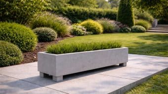 Donica ogrodowa Francesco 9, wypełniona wysoką zieloną trawą, stoi na wybrukowanym patio pośród przyciętych krzewów i wypielęgnowanej trawy. Schody w tle prowadzą w górę przez bujną zieleń przy delikatnym świetle dziennym.