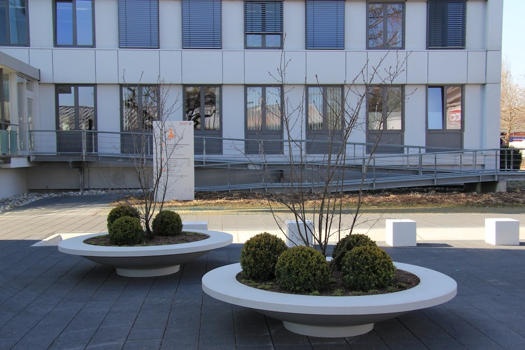 Dwie duże donice o kształcie misy umieszczone przed wejściem do biurowca