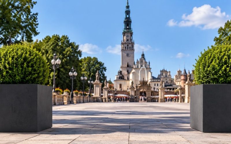 Czarne donice betonowe z bukszpanem – Częstochowa, Jasna Góra Dwie czarne kwadratowe donice betonowe z kulistym bukszpanem na tle Jasnej Góry w Częstochowie.