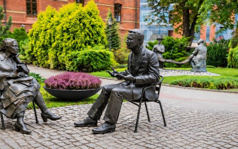 Donica Agnese z wrzosem w ogrodzie rzeźb Czarna okrągła donica Agnese z wrzosem obok plenerowych rzeźb